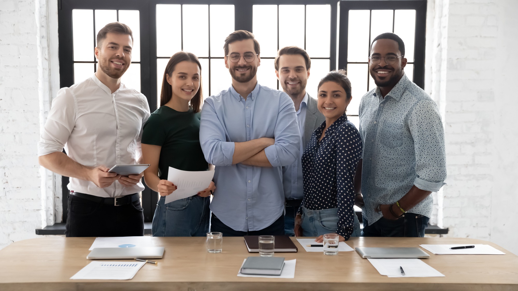 Corporate photo smiling diverse employees with confident executive wearing glasses standing in modern office room,